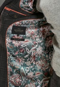 Veste à carreaux foncée avec doublure à motifs floraux en bleu sarcelle, crème et bordeaux. Comprend une étiquette "next" pour la taille 40R et des détails de coupe régulière.