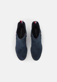 Botas de tobillo de ante azul marino con una textura suave, que presentan un acento en rojo, blanco y azul en el talón y un detalle redondo de logo en plata.