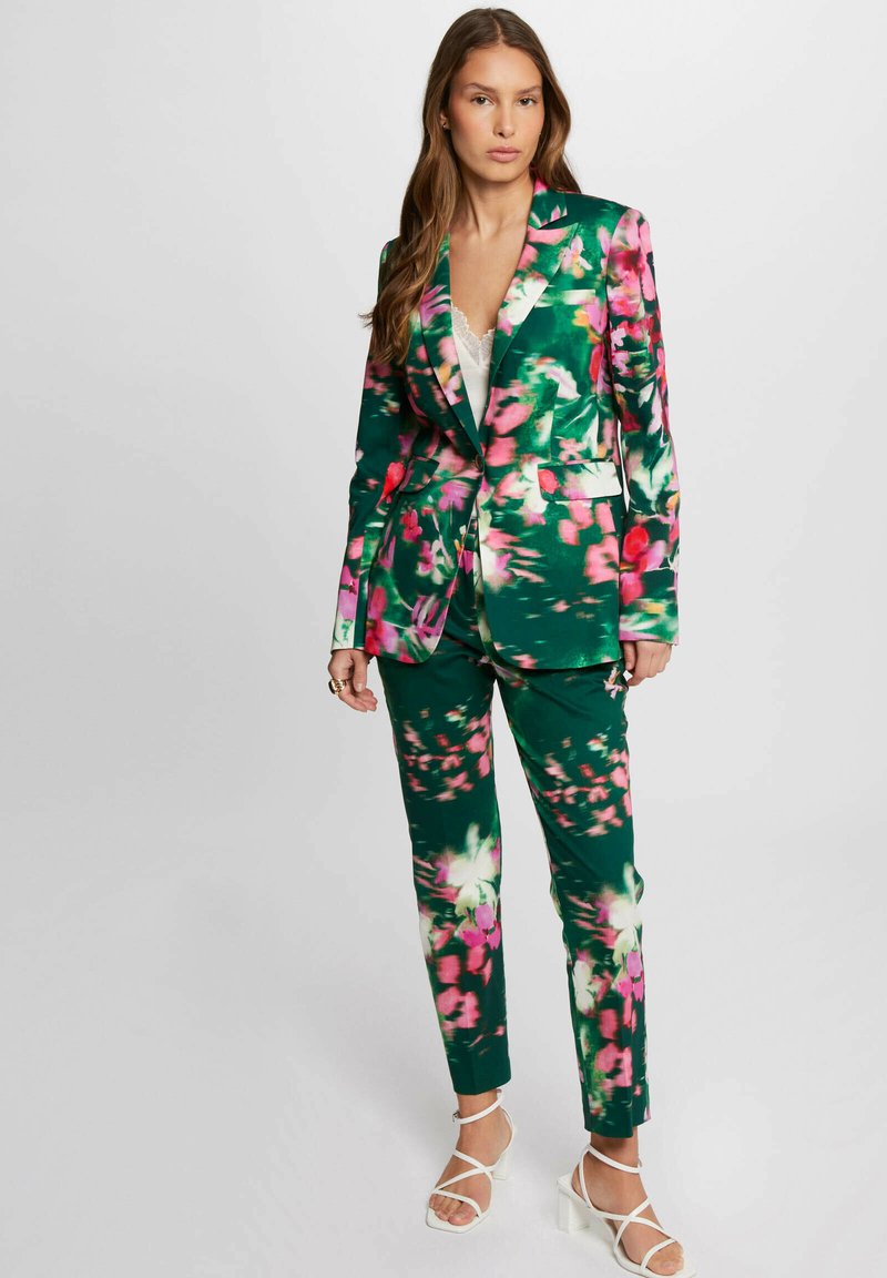 Completo floreale verde con motivi rosa e bianchi, giacca su misura con rever a punta e pantaloni abbinati, abbinato a tacchi bianchi con cinturini.