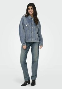 Giubbotto di jeans in blu chiaro con una vestibilità rilassata, caratterizzato da tasche sul petto, bottoni argentati e maniche lunghe, abbinato a jeans a gamba dritta.