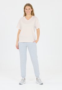Korte mouwen, lichtbeige V-hals T-shirt gecombineerd met grijze sweatpants. De stof lijkt zacht, met een ontspannen pasvorm en zijvakjes. Casual schoenen.
