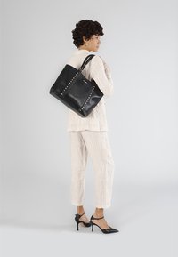 Borsa tote in pelle nera con accenti di borchie argentate, forma rettangolare grande, doppie spalline e chiusura superiore con zip.