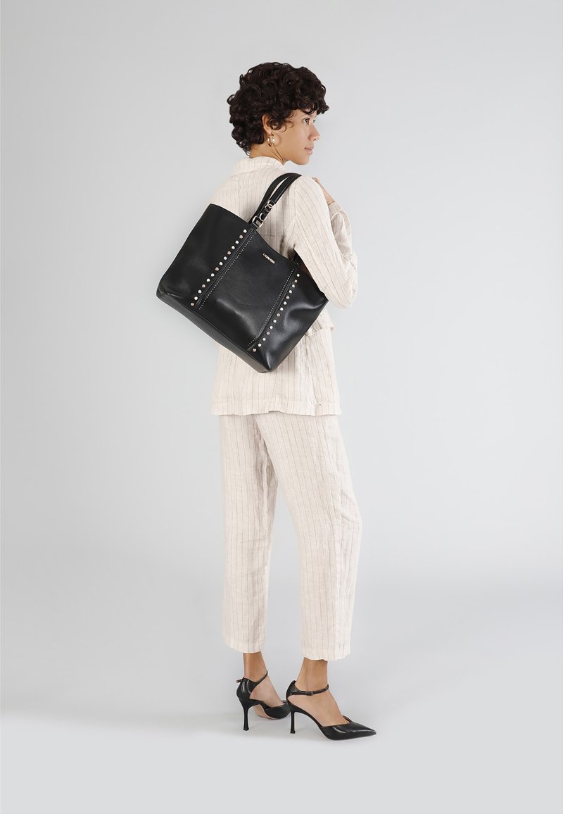 Borsa tote in pelle nera con accenti di borchie argentate, forma rettangolare grande, doppie spalline e chiusura superiore con zip.