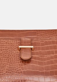 Brown leather bag with crocodile pattern texture, featuring a gold-tone metal clasp and a rectangular leather strap closure.