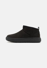 Botines de ante negro con suela de goma texturizada, que presentan acentos cosidos y una lengüeta en la parte posterior para facilitar su uso.