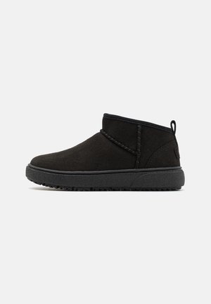 Botines de ante negro con suela de goma texturizada, que presentan acentos cosidos y una lengüeta en la parte posterior para facilitar su uso.