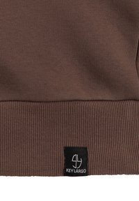 Sudadera de tela acanalada marrón con una etiqueta negra "Key Largo" en la parte inferior izquierda. El material parece suave y texturizado.