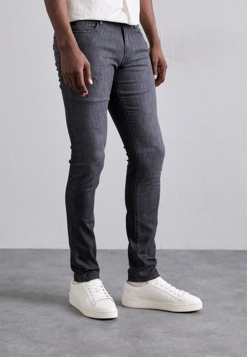 Grå denimjeans med slim fit, med fem fickor och minimal söm. Bärs med vita sneakers för kontrast mot golvet.