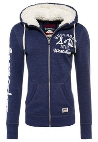 Felpa con zip blu navy, con un interno bianco soffice, dotata di un logo sul petto, cappuccio con cordino e tasche frontali. Polsini e orlo a coste.