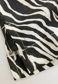Zwart-wit zebraprint stof met een zachte textuur en zichtbare stiksels, die golvende patronen en een afgewerkte rand toont.