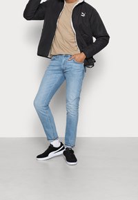 Sort bomberjakke med hvidt pelsfor, beige t-shirt, lyseblå slim-fit jeans og sorte sneakers med hvide såler. Enkel, moderne stil.