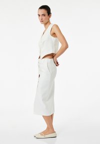 Witte cropped mouwloze blouse met een V-hals en knopen, gecombineerd met een bijpassende rok tot de knie. Gladde textuur en strakke lijnen.