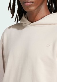 Light beige hoodie with a soft texture, featuring a kangaroo pocket and a small embroidered logo on the chest, minimalistic design.