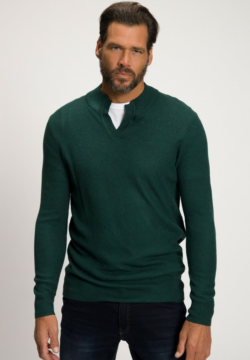 Maglione a maglia verde scuro con scollatura a V e finitura testurizzata. Maniche lunghe e vestibilità rilassata, abbinato a jeans di denim scuro.