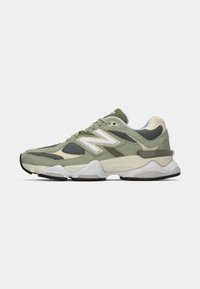 Baskets de sport New Balance vertes et grises avec des accents blancs, des panneaux en maille et une semelle épaisse et rembourrée, montrées de côté gauche.