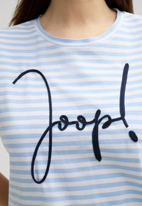 Lichtblauw en wit gestreept T-shirt met een ronde hals, voorzien van donkerblauwe geborduurde tekst "Joop!" op de voorkant. Zachte katoenmateriaal.