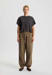 Lyhythihainen harmaa t-paita, jossa on kapea leikkaus, yhdistettynä väljiin oliivinvihreisiin housuihin, joissa on joustava vyötärö ja lahkeet. Mustat litteät kengät.