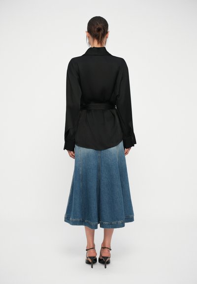 Black satin long-sleeve blouse with a tie belt at the waist, paired with a mid-length, flared blue denim skirt and strappy black heels.