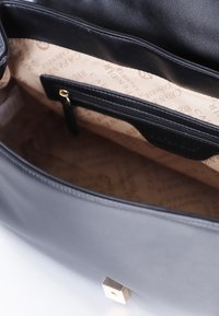 Sort læder håndtaske åben for at vise beige indvendig foring med gentagne "CAPENOIR"-logoer og en lille lynlås lommer.