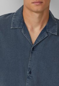 Blauw gemusterde overhemd met korte mouwen en een gespreide kraag, met textuurdetails en een knoopsluiting. Zacht stof met een subtiele glans.