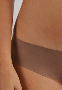 Sous-vêtements bruns sans coutures avec une bande douce, une texture lisse et un design minimaliste. La ceinture s'ajuste confortablement contre la peau.