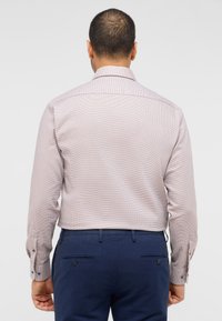 Heren langemouwen overhemd in lichtroze met een subtiel geometrisch patroon, voorzien van een spread collar en knopenmanchetten. Gecombineerd met een marineblauwe broek.