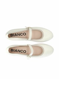 Bailarinas blancas con puntera redonda, con tira tipo Mary Jane y interior beige. Están hechas de un material suave con un diseño mínimo.