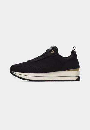 Black low-top sneaker with mesh upper, white thick sole, gold heel accent, pull tab at heel, and black laces with gold eyelet.