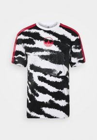 Kortärmad t-shirt i vitt med ett svart och grått zebraliknande mönster, röda axelremmar och en rund logo i mitten.