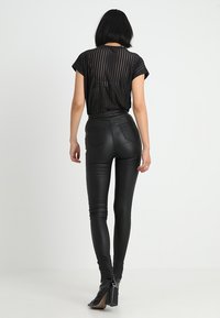 Top negro, transparente, con rayas verticales, combinado con leggins negros de cintura alta. Los leggins cuentan con bolsillos traseros y una textura suave y similar al cuero.