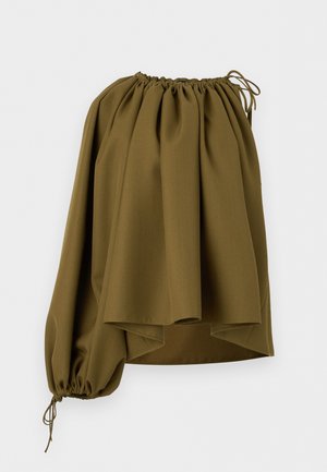 Γυναίκα που φοράει ελιά πράσινο τοπ με ένα φουσκωτό μανίκι, καρό φούστα με μεγάλο πλάγιο άνοιγμα και μαύρα πέδιλα με λουριά και τακούνι.