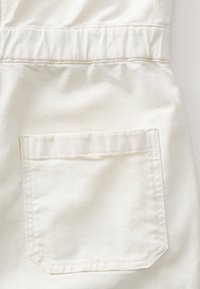 Tissu en coton blanc d'un vêtement avec une poche cousue aux bords droits et une texture subtile, sur fond neutre.