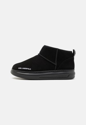 Black suede ankle boots with a rounded toe, featuring signature branding and a contrasting rubber sole with a pull tab at the back.