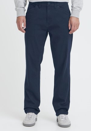 Pantalon en coton mélangé bleu marine, coupe droite, avec une texture lisse, doté d'une fermeture à bouton et de poches avant. Porté avec des baskets blanches.