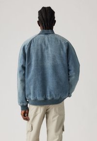 Chaqueta bomber de mezclilla en azul claro con puños y dobladillo de canalé. Presenta un ajuste relajado y mangas ranglán, diseñada para un look casual.