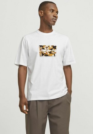 T-shirt en coton blanc avec un graphic carré présentant un motif floral éclatant en orange, noir et blanc, associé à un pantalon gris ample.
