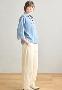 Camicia in denim azzurro chiaro con scollo a V e maniche a tre quarti, abbinata a pantaloni cream a gamba ampia. Le scarpe sono a tacco basso con perforazioni.