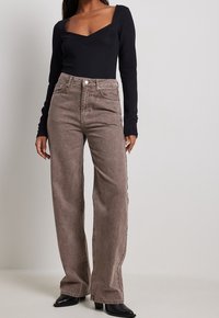 Bodysuit noir à manches longues avec un décolleté carré, associé à un jean marron taille haute à jambes larges, comportant des poches arrière et une fermeture à bouton.