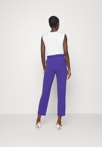 Top in maglia bianca aderente con maniche corte abbinato a pantaloni viola a vita alta. I pantaloni presentano una vita arricciata e un design a gamba dritta.