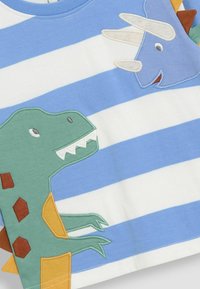 Mėlynos ir baltos juostelės tekstilė, kurioje yra siuvinėtas žalias dinozauras ir mėlynas triceratopsas, su oranžinėmis ir rudos spalvos akcentais ant žalio dinozauro.