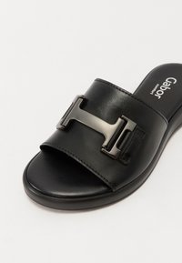 Sorte slide sandal med en bred stropp og en skinnende sølv-tone hardwaredetalj. Glatt lærøverste med polstret fotseng.