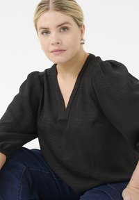 Czarna bluzka z dekoltem w serek, puffowanymi rękawami 3/4, teksturowanym materiałem i luźnym krojem, zestawiona z niebieskimi dżinsami.