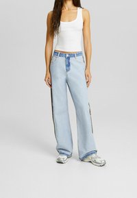 Ljust blå vida jeans med kontrasterande blå panel vid midjan och bruna sidostrickor. Avslappnad passform och fransade fållar.