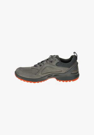 Grijze sportieve schoen met een gestructureerde suède en mesh bovenkant, voorzien van een zwarte kraag en een oranje rubberen zool voor grip. Vetersluiting.