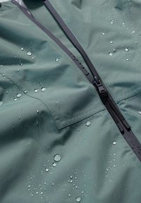 Giacca resistente all'acqua in tessuto verde scuro. Presenta una cerniera centrale nera, una superficie testurizzata con gocce d'acqua e una tasca sul petto.