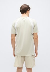 Αθλητική μπλούζα σε ανοιχτό μπεζ χρώμα με λευκά raglan μανίκια, διακοσμημένη με μαύρες και μπεζ λεπτομέρειες· συνδυάζεται με ταιριαστό σορτς, με ομαλή υφή.