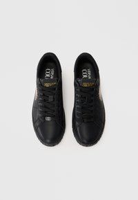 Melni ādas sporta apavi ar gludu tekstūru, apaļu purngalu, platiem šņorēm, ar zīmolu uz mēles un zelta akcentu sānos.