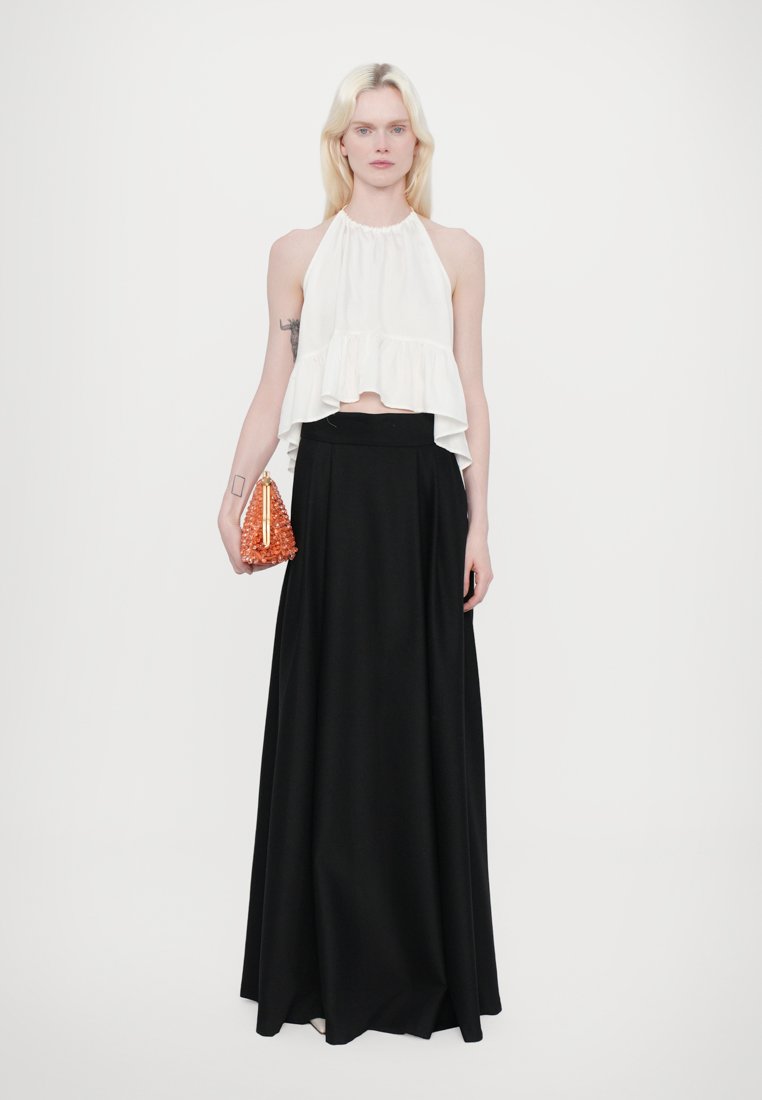 Haut halter blanc avec un ourlet à volants, associé à une longue jupe noire. Le mannequin tient un sac à main en perles orange avec un fermoir en or.