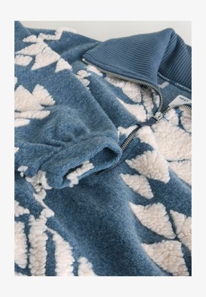 Zils flīsa krekls ar ribotu apkakli, ar krēmīgu ģeometrisku rakstu. Iekļauj zipa aizdari un mīkstu, teksturētu audumu.