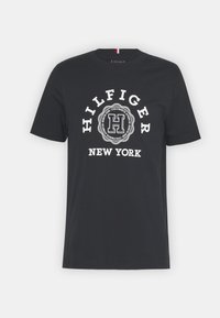 Černé bavlněné tričko s bílým kulatým logem a textem "HILFIGER" a "NEW YORK". Krátké rukávy a kulatý výstřih, hladká textura.